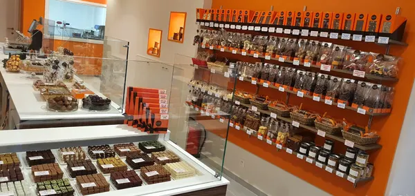 La boutique Chocolate Temptation : vitrine de pralines et murs orange garnis de tablettes